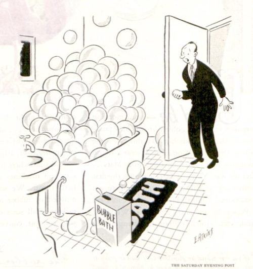 A man stands in a bathroom doorway. The bathtub is full of large soap bubbles. The wife is underneath the bubbles taking a bubble bath