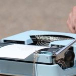 A typewriter on a table with a sign reading "Poet for Hire"