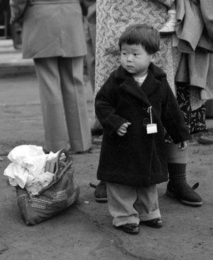 Japanese boy in a coat standing with people. A basket rests next to him.
