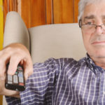 Older man flipping through television channels with his remote.