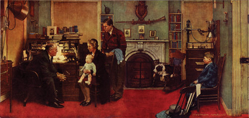 A family visits a doctor at his home office. He sits at his desk while he speaks to the family; the mother sits in the chair in front of him while holding her baby.