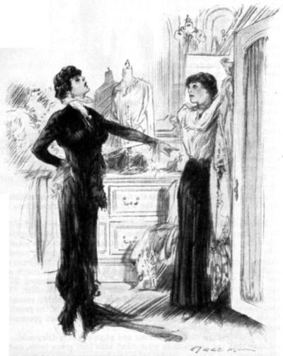 Woman in a black dress speaks to another; the other woman is putting up clothes onto a hanger.