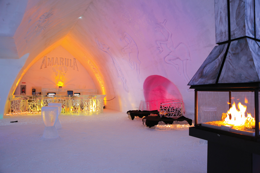 The interior of a bar made out of an igloo, complete with drinks, ice chairs, and a fireplace.