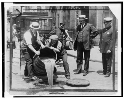 Law enforcement agents pour a barrel of liquor into an open sewer hole following a prohibition raid.