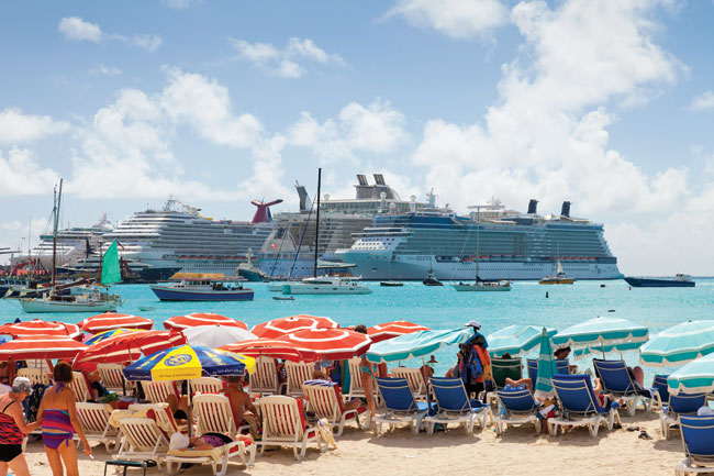 people under umbrellas on sand looking out at cruise ship on the ocean