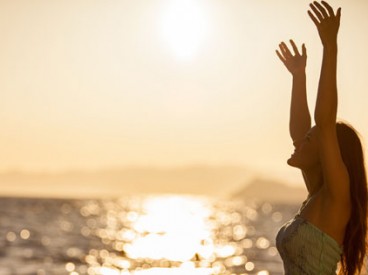 Young, happy woman on a beach at sunset, raising her hands in the air