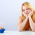 Young woman staring sadly at a birthday cupcake. Source: Shutterstock.com / Doreen Salcher