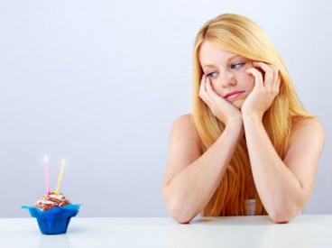 Young woman staring sadly at a birthday cupcake. Source: Shutterstock.com / Doreen Salcher