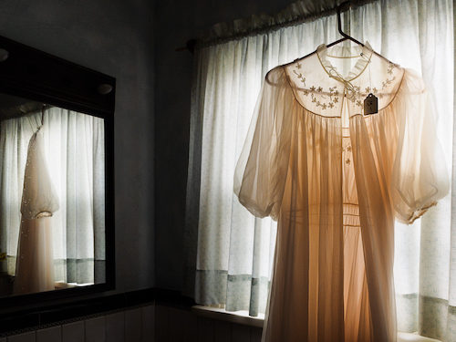 A pink negligee hangs on a curtain rod in a darkened room