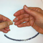 hands holding beads, crimp bead, and magnetic clasp on wire
