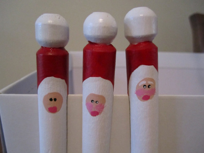 Santa faces painted on wooden clothespins hanging on shoebox
