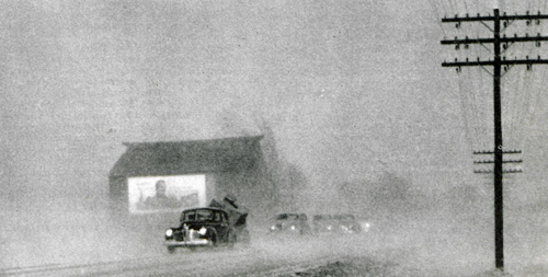 Cars drive through a dust storm in the late 1940s.