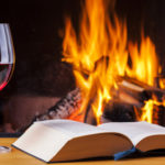 book and full wineglass in front of fireplace