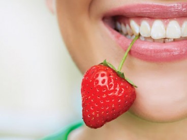 Young woman holding a strawberry between her teeth by its stem. Source: Shutterstock.com