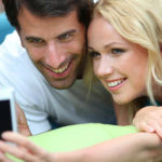 Couple taking pictures of themselves with mobile phone. Courtesy of Shutterstock.