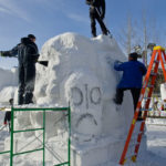 three people carving snow sculpture