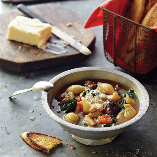 Boul of soup on a table with bread on a cutting block.