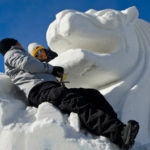 people climbing up and carving snow-sculpted lion