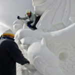 people climbing on snow-sculpted lion to carve
