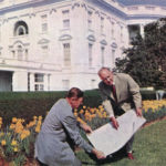 Two men looking at plans in front of White House