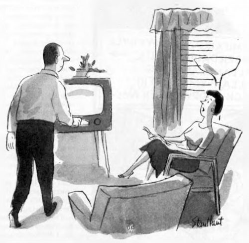 Woman sits in chair, reading. Husband is at the TV, about to turn it on.