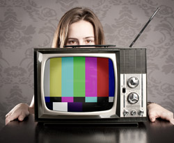 A woman sitting behind a television set. The screen is displaying a call pattern.