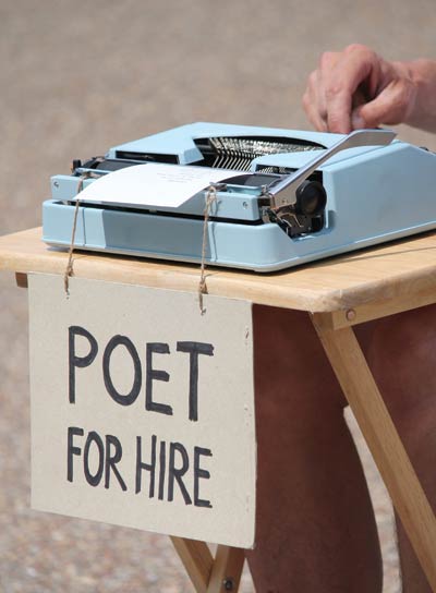 A typewriter on a table with a sign reading "Poet for Hire"