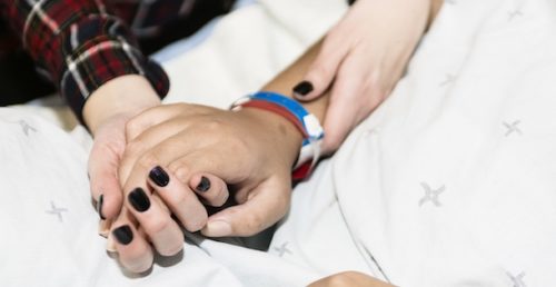 A woman holder her dying parent's hand