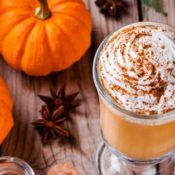 Pumpkin spice latte next to pumpkins on a wooden table