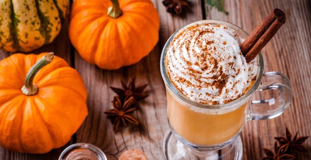 Pumpkin spice latte next to pumpkins on a wooden table