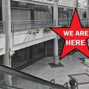 The interior of an abandoned mall. A star with the message "We Are Here" is superimposed over it