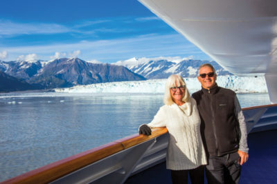 Steve and Estelle Slon on a ship deck with the Hubbard Glacier in the distance