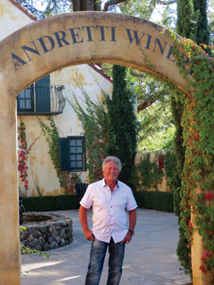 Mario Andretti standing in front of a sign for "Andretti Winery"