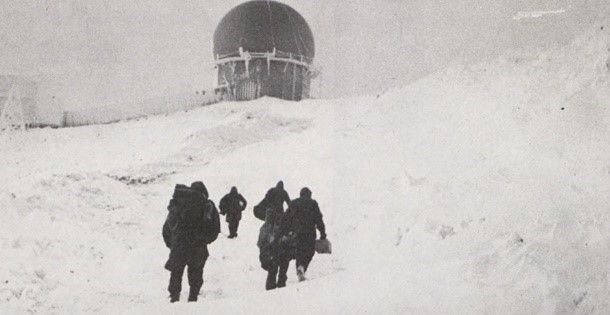 Men walking to a radar attenae in the snow