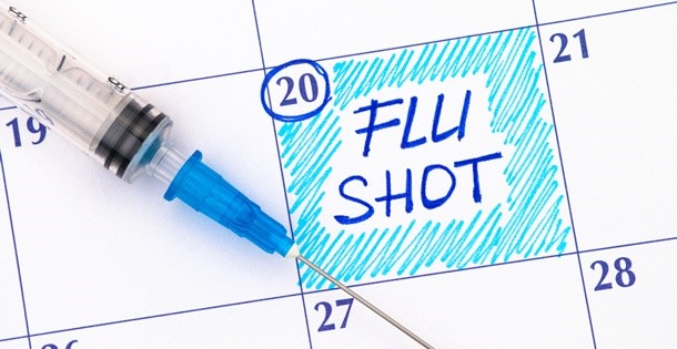 Calendar with a date marked "flu shot: and a syringe needle laying atop it.
