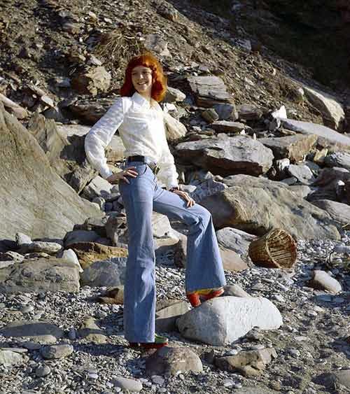 A model wearing denim bell bottoms on a rocky shore.