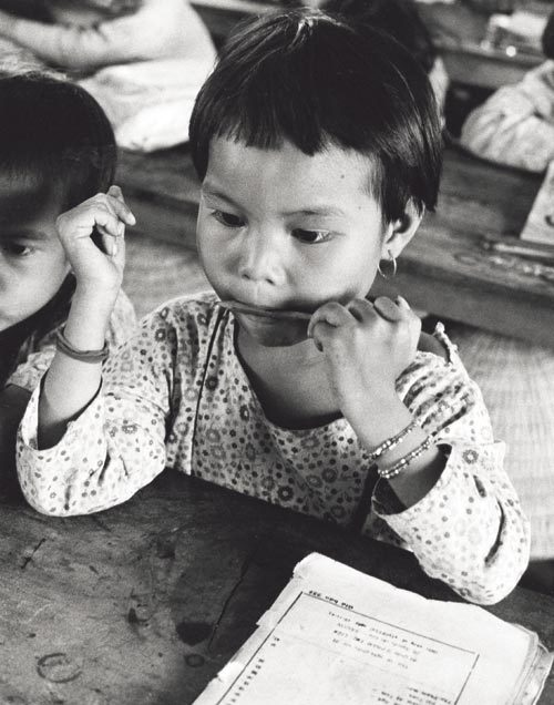 Vietmese girl chewing on a pencil at her school desk.