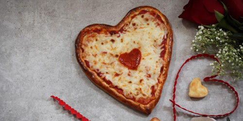 A pizza shaped like a Valentine's heart. A single, heart-shaped pepperoni is its topping. 