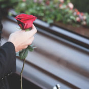 A woman holding a rose in front of a casket at a funeral.