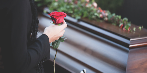 A woman holding a rose in front of a casket at a funeral.