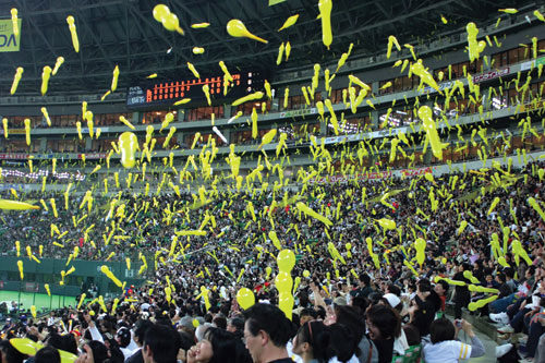 Photo of Japanese spectators launch balloons into the air at the end of a baseball game.