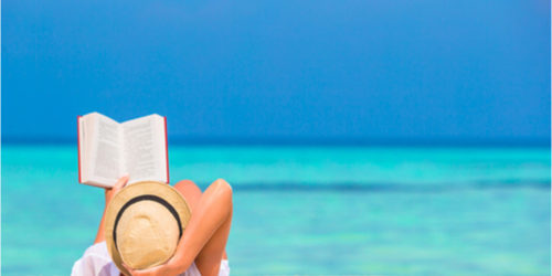 Woman reading a book while laying on the beach