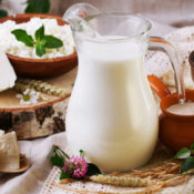An assortment of dairy items on a kitchen table. They include a pitcher of milk and a variety of cheese.
