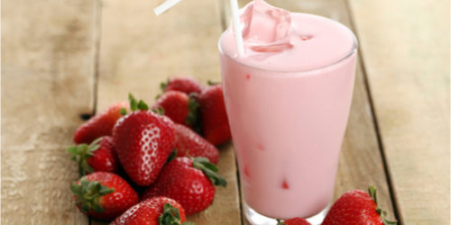 Strawberry cocktail in a glass, with strawberries, on a wooden table.