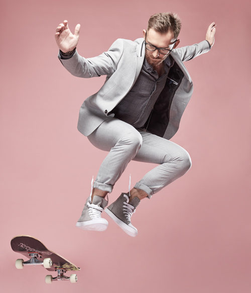 Man in business-casual attire performs a trick on a skateboard.