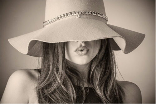 A woman model wearing a wide brim hat that covers her eyes. She is making a kissing face.
