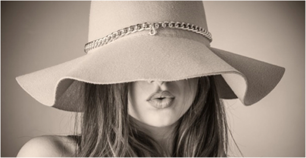 A woman model wearing a wide brim hat that covers her eyes. She is making a kissing face.