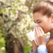 Woman blowing her nose in front of a tree.