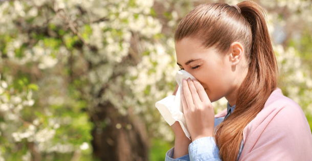 Woman blowing her nose in front of a tree.