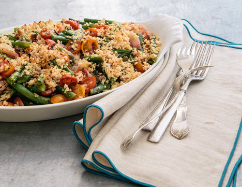 A plate of Curtis Stone's Green Bean and Tomato Gratin next to silverware.